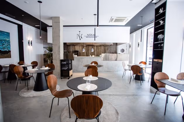 Sala del restaurante con mesas redondas y la cocina abierta al fondo